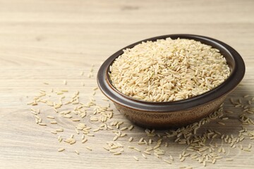 Brown rice in bowl on wooden table, closeup. Space for text