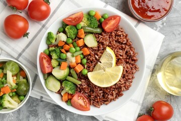 Delicious brown rice with vegetables and lemon slices served on grey textured table, flat lay