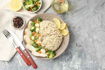 Delicious brown rice with chicken, vegetables and lemon slices served on grey textured table, flat lay. Space for text