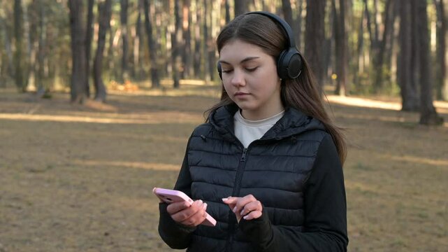Jogging girl in forest receives message and feels arrogant during reading. A girl jogging through a forest pauses to read a message on her phone, exuding confidence and contempt