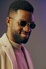 Obraz premium Stylish African man wearing sunglasses and a fashionable coat smiles confidently against a pastel colored background, capturing modern elegance and confidence