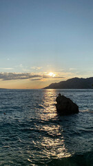 A confident man sits on the edge of a rocky cliff, preparing for an exhilarating dive into the deep...