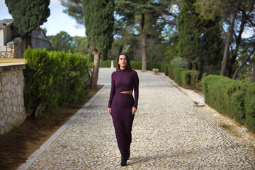 Young, beautiful, brunette, Hispanic woman, wearing a purple dress and high heels, walking alone on...