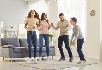 Fototapeta premium Full length portrait of young happy family of mother,father and two kids having fun and dancing in the living room at home. Parents enjoying spending time with children. Family leisure concept