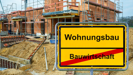 Obraz premium Ein Ortsschild mit der Aufschrift Bauwirtschaft und Wohnungsbau steht vor der Baustelle von Wohnhäusern und Mietwohnungen - Symbolbild - FOTOMONTAGE