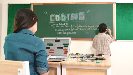 Girl writing engineering prompt by using AI software or programing system to generate AI on table with electronic main board at stem class while smart boy writing software development plan. Pedagogy.
