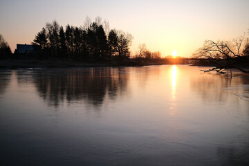 Obraz premium Colorful morning sunrise, ice covered river without snow, reflection of trees and sun on smooth mirror ice surface. Vircava river, Jelgava town, Latvia