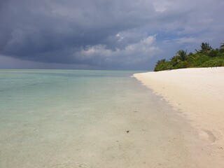 Pristine Beach and Crystal Waters Under Stormy Skies in Maldives