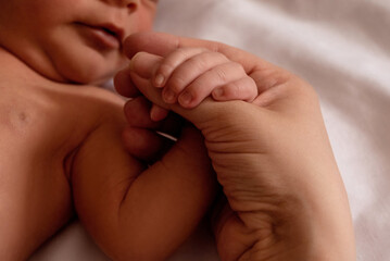 Newborn baby tenderly holds mother's finger