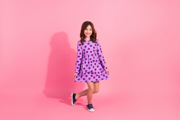 Charming pretty girl in a stylish polka dot dress against a pastel pink background showcasing fashion and trendy casual wear for kids.
