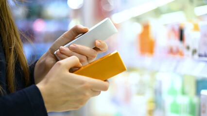 A female customer reading the ingredient labels compares two Skincare or Beauty products. Close-up...