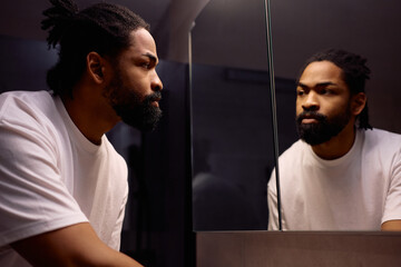 Black man looking himself in mirror in bathroom.