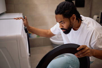 Mid adult black man using washing machine at home.