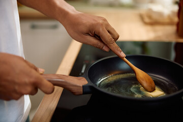 Close up of black man melting butter while preparing food in frying pan.