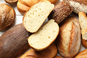 Whole and cut bread loafs on white wooden table, flat lay