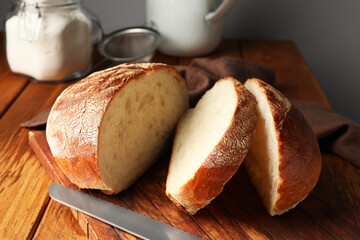 Cut loaf of fresh bread and knife on wooden table, closeup
