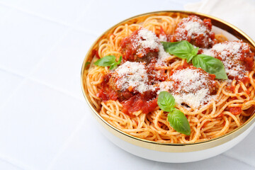 Delicious pasta with meatballs, cheese and basil in bowl on white tiled table, closeup. Space for text