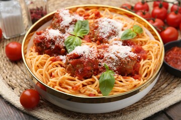 Delicious pasta with meatballs, cheese and basil in bowl on wooden table, closeup