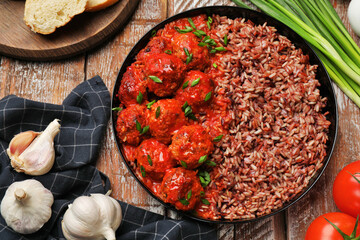 Tasty meatballs with sauce, brown rice and products on wooden table, flat lay