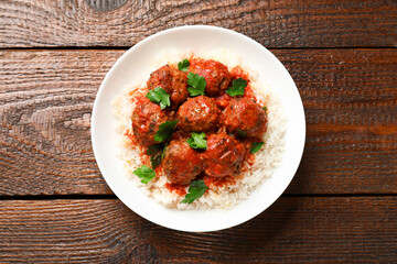 Tasty meatballs with sauce and rice on wooden table, top view