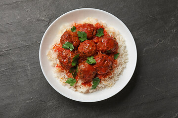Tasty meatballs with sauce and rice on black table, top view