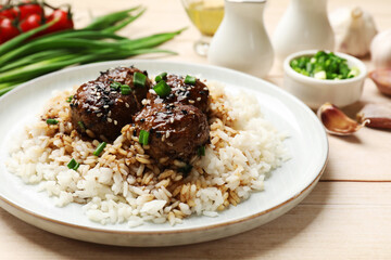 Delicious rice with meatballs, sauce and green onions on white wooden table, closeup