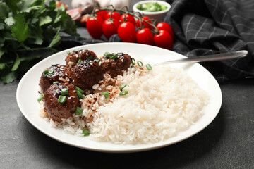 Delicious rice with meatballs, sauce and green onions on black table, closeup