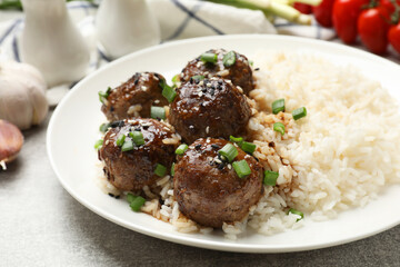 Delicious rice with meatballs, sauce and green onions on grey table, closeup