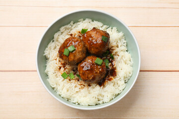 Delicious rice with meatballs, sauce and green onions in bowl on white wooden table, top view