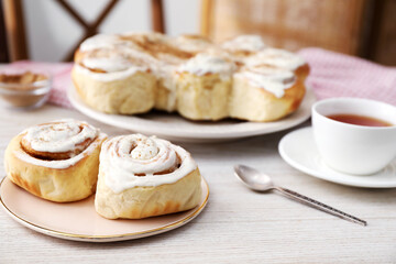 Delicious frosted cinnamon rolls on light wooden table, closeup