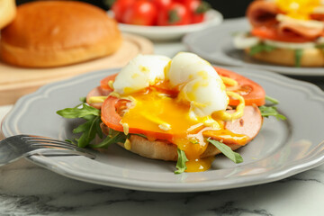 Tasty brunch. Poached egg, ham, tomato, arugula and bun on white marble table, closeup