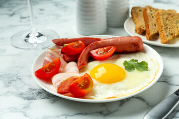 Tasty brunch. Fried egg, sausage, bacon and tomatoes on white marble table, closeup