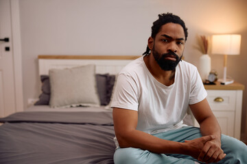 Distraught black man sitting on bed and looking at camera.