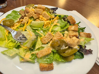 Salad with lettuce, croutons, cucumbers and jalapenos on a white plate with a fork, ready to eat