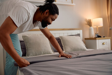 Happy black man making his bed in morning.