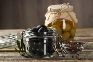 Pickled olives in glass jars and spices on wooden table, closeup