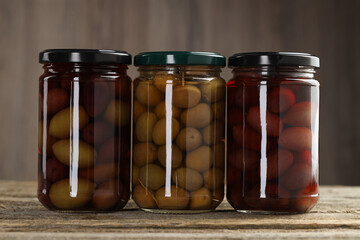 Pickled olives in glass jars on wooden table