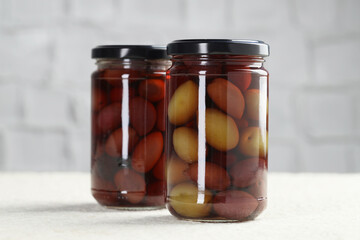 Pickled green olives in jars on white textured table, closeup