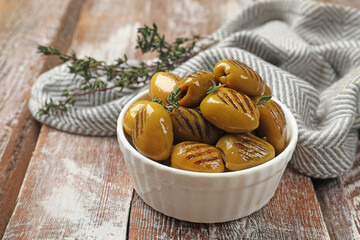 Grilled green olives with thyme in bowl on wooden table, closeup