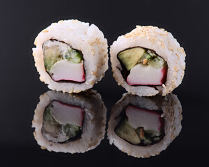 Two california sushi rolls with sesame seeds reflecting on dark background