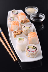 Delicious sushi rolls with soy sauce and mayonnaise on black background