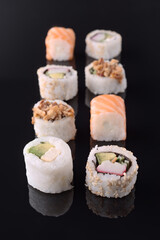 Variety of delicious sushi rolls displayed on black reflective surface
