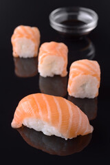 Salmon nigiri and maki sushi with soy sauce on black reflective background