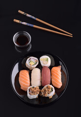 Delicious sushi assortment with soy sauce and chopsticks on black background