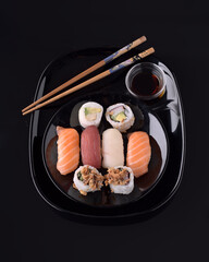 Delicious sushi assortment with soy sauce and chopsticks on black background