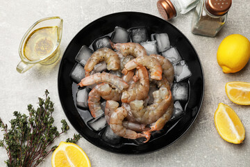 Fresh raw shrimps with ice cubes in bowl, spices and lemons on grey table, flat lay