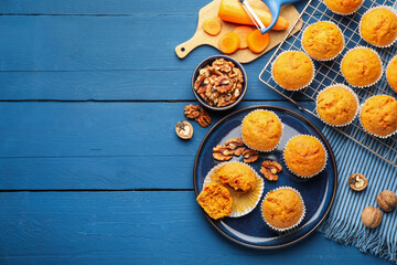 Tasty carrot muffins, walnuts and fresh vegetables on blue wooden table, flat lay. Space for text
