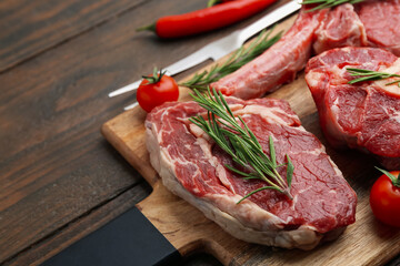 Pieces of raw beef, rosemary and tomatoes on wooden table, closeup. Space for text