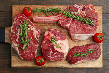 Pieces of raw beef, rosemary and tomatoes on wooden table, top view