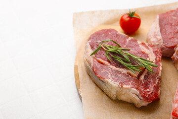 Pieces of raw beef, rosemary and tomato on white tiled table, closeup. Space for text